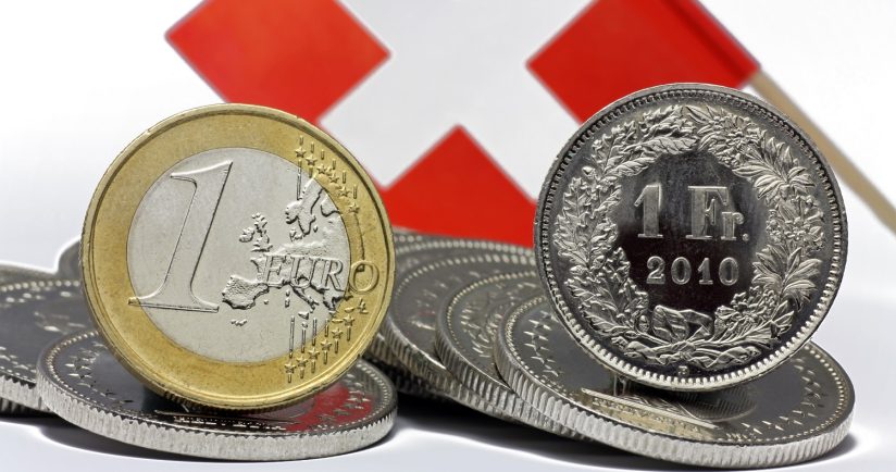 Euro- und Franken-Münze vor Schweizer Flagge.