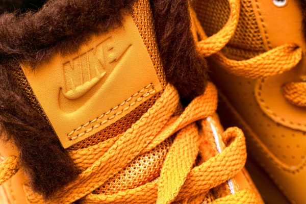 Detailansicht eines gelben Sneakers mit braunem Kunstfell und gesticktem Logo.