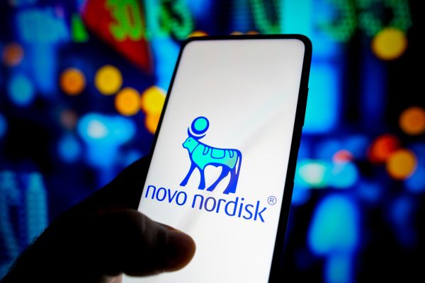Smartphone mit Novo Nordisk Logo in der Hand vor verschwommenem, buntem Hintergrund.
