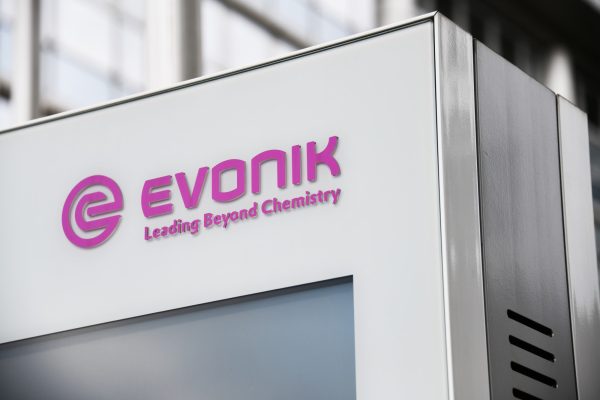 Schild mit lila Evonik-Logo und dem Schriftzug "Leading Beyond Chemistry". Hintergrund aus Glas.