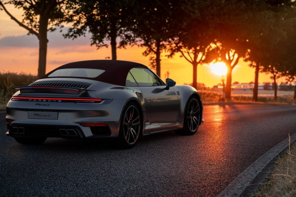 Silbernes Auto auf Landstraße bei Sonnenuntergang, umgeben von Bäumen.