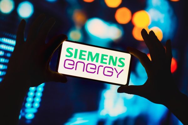 Hände halten ein Smartphone mit Siemens Energy Logo vor unscharfem Hintergrund.